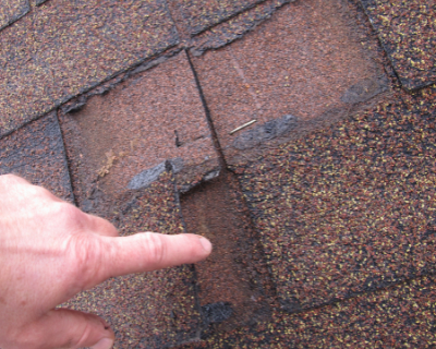 Roof Repair Services | What Causes Roof Damage - a hand pointing a finger to missing and damaged asphalt shingle roof