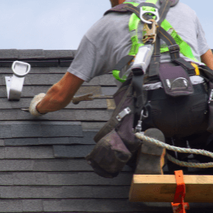 roofing companies near me - The Benefits of Hiring a Professional Roofing Contractor for Your Roofing Project - a roofer with a harness on scaffolding replacing missing shingles