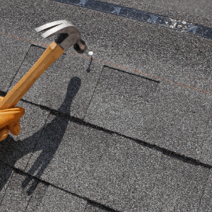 roofing companies Kingsport TN - The Services Roofing Companies in Kingsport TN Provide - a hand with a hammer hitting a nail on an asphalt roofing tile
