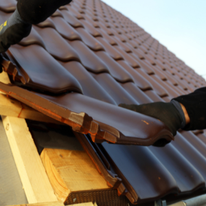 replacing a roof - a pair of roofer's hand attaching the last clay tile on a roof